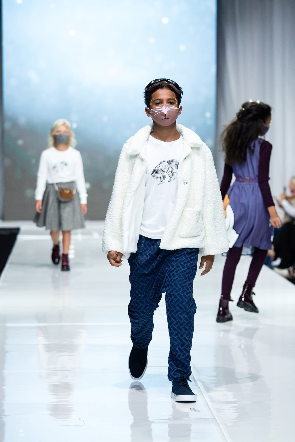 Child walks the runway wearing their lorek t-shirt, northern jacket, subtle knife joggers, and mask