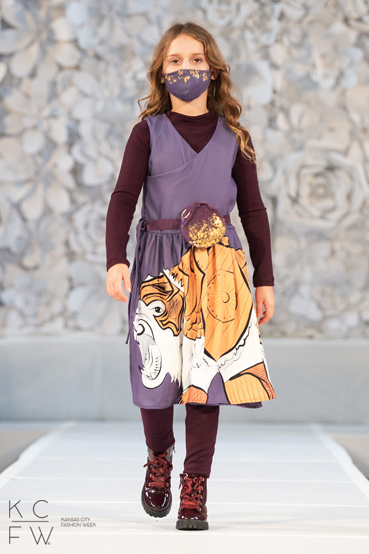 Young lady walks the runway in her lorek dress, purple rib knit tunic and leggings, mask and bag