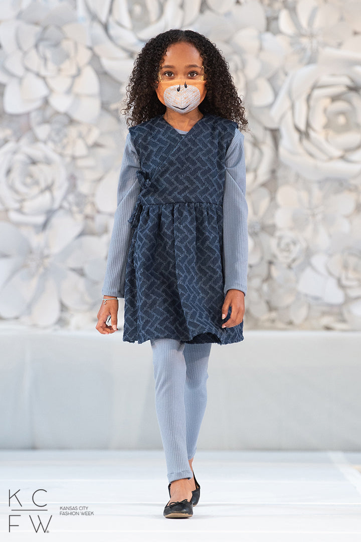 A beautiful young girl on the runway in her subtle knife dress over blue knit leggings and tunic