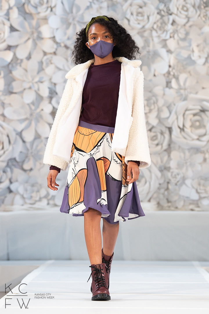 A young lady walks the runway pairing her purple knit tunic with her northern jacket and lorek skirt