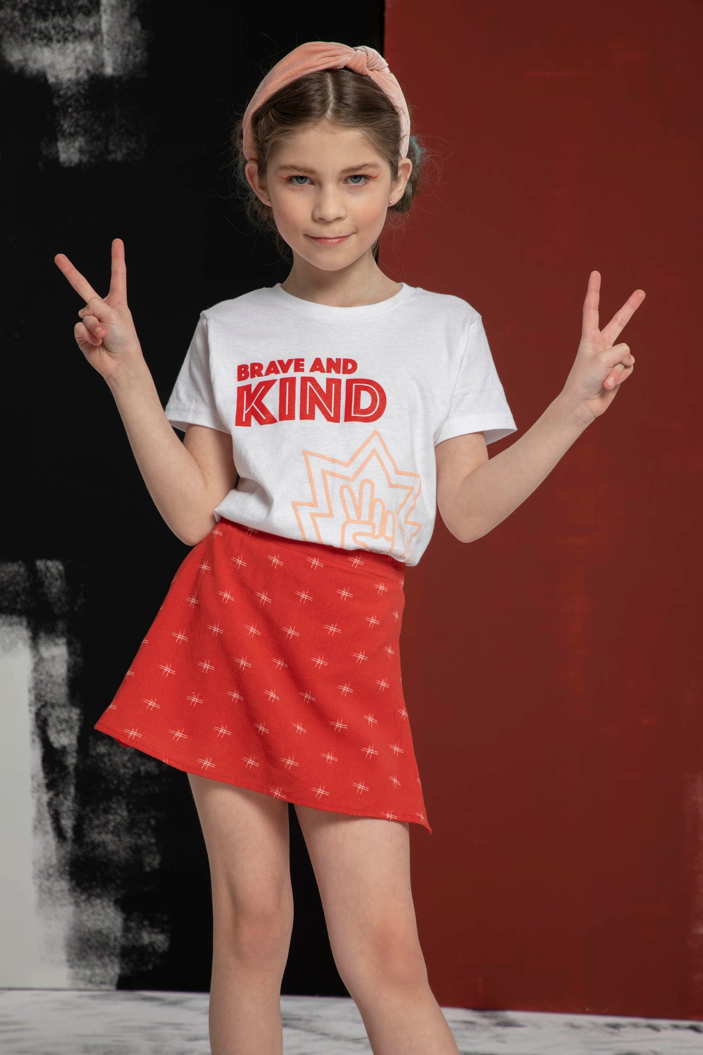 Leaning to the side and smile on the camera a girl poses with double peace signs in her shirt