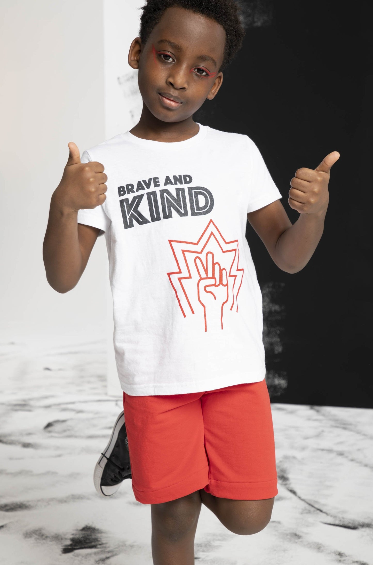 Young boy puts both thumbs up and a lef back to being brave in kind in his t-shirt and chief shorts