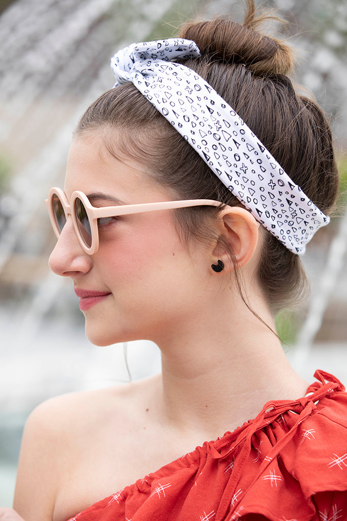 A profile shot outside displays a girl wearing her crescent earrings, sunnies, and headband in a bun