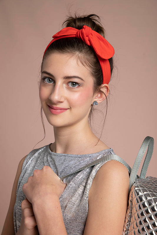 A lovey headshot of a girl shows her wearing the red headband along side her metallic backpack