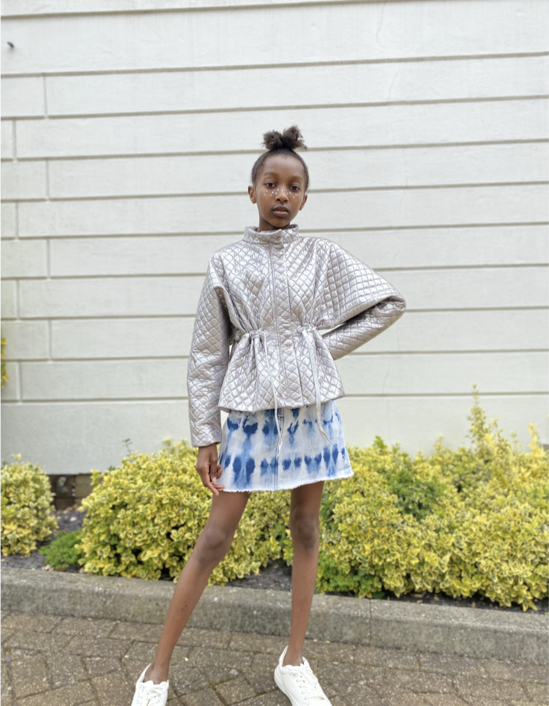 Maya Glitters poses outside in the Atari Jacket along with her shibori dyed skirt and white shoes