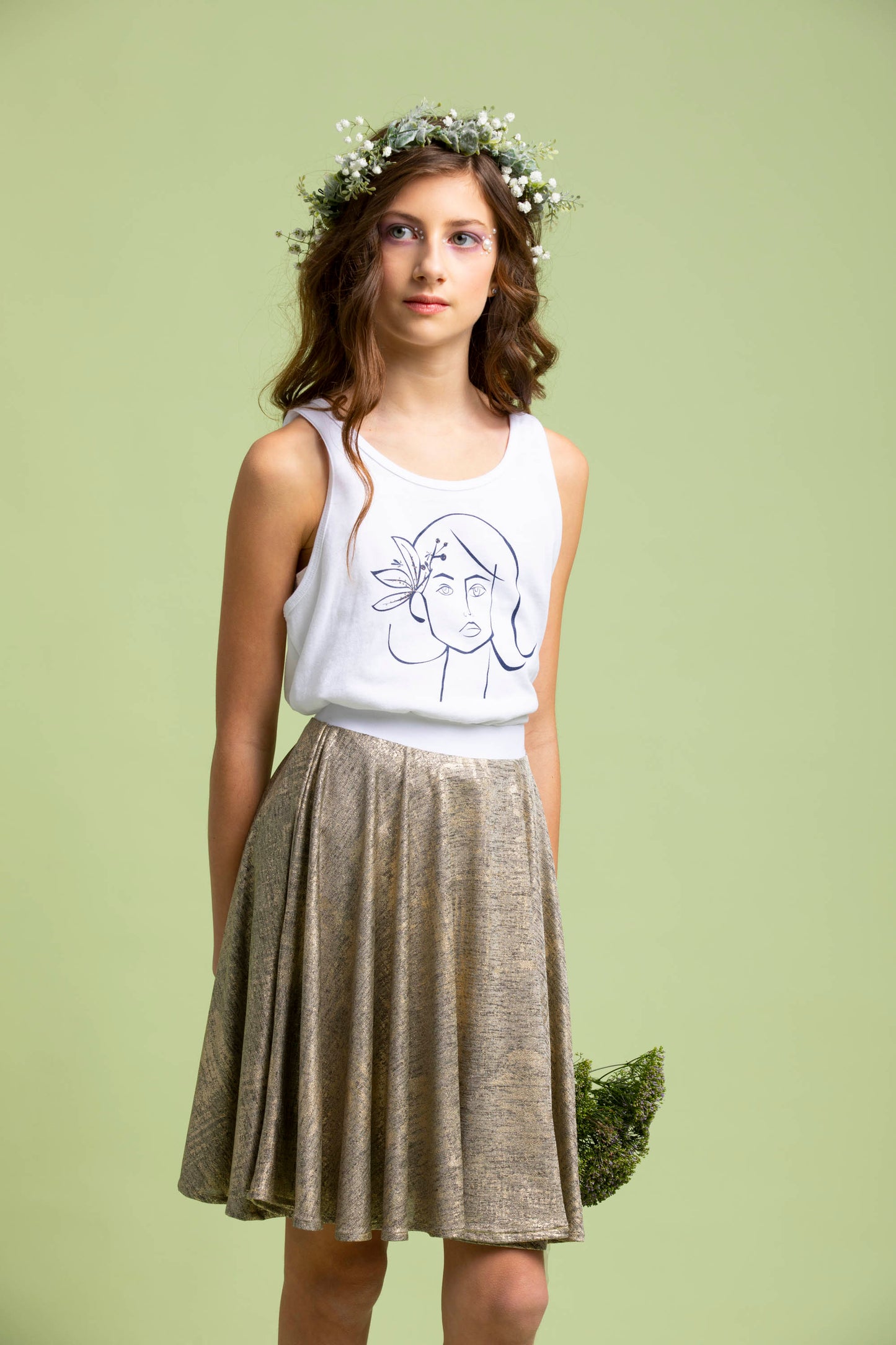 Holding some greenery behind her, a young lady wears her gold knit Mercedes Skirt and Ofelia T-Shirt