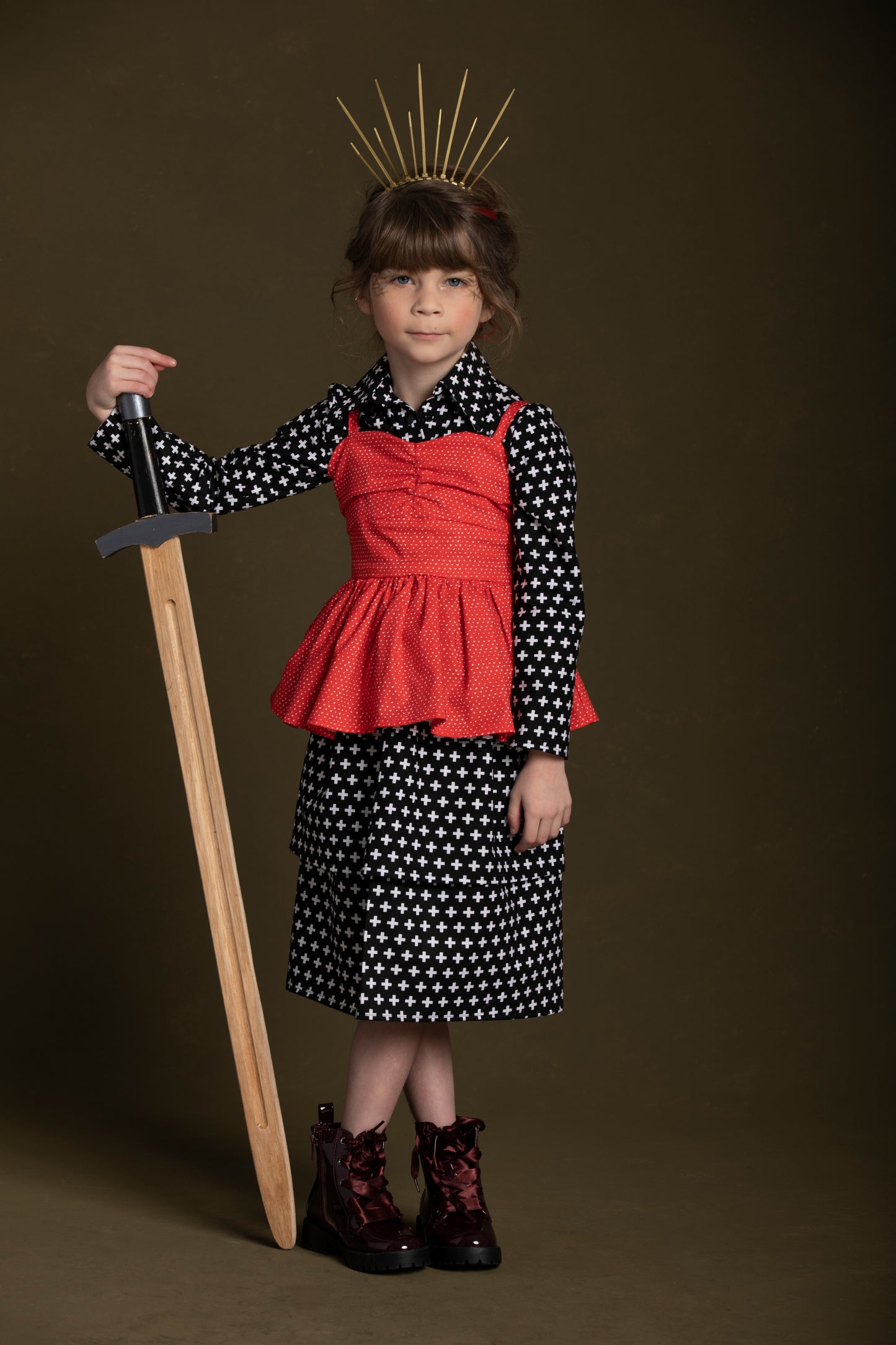 Young girl rests on her sword while layering her red heart peplum top over a plus print shirt dress