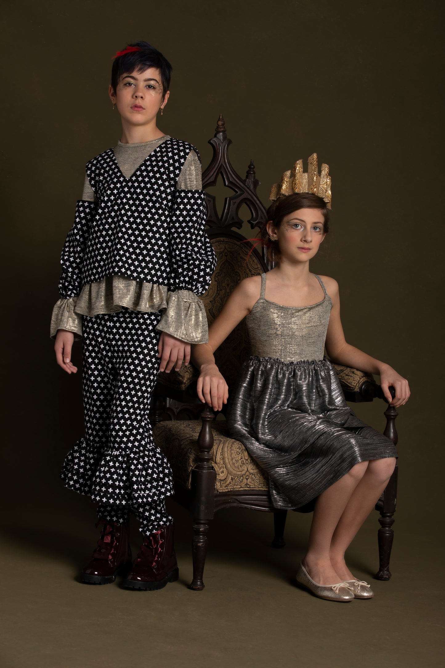 Child wearing the plus print off-shoulder top stands next to another child who sits in her throne