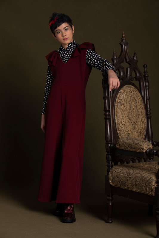 Young lady rests her arm on a chair in her burgundy knit jumpsuit with a snap down top under it