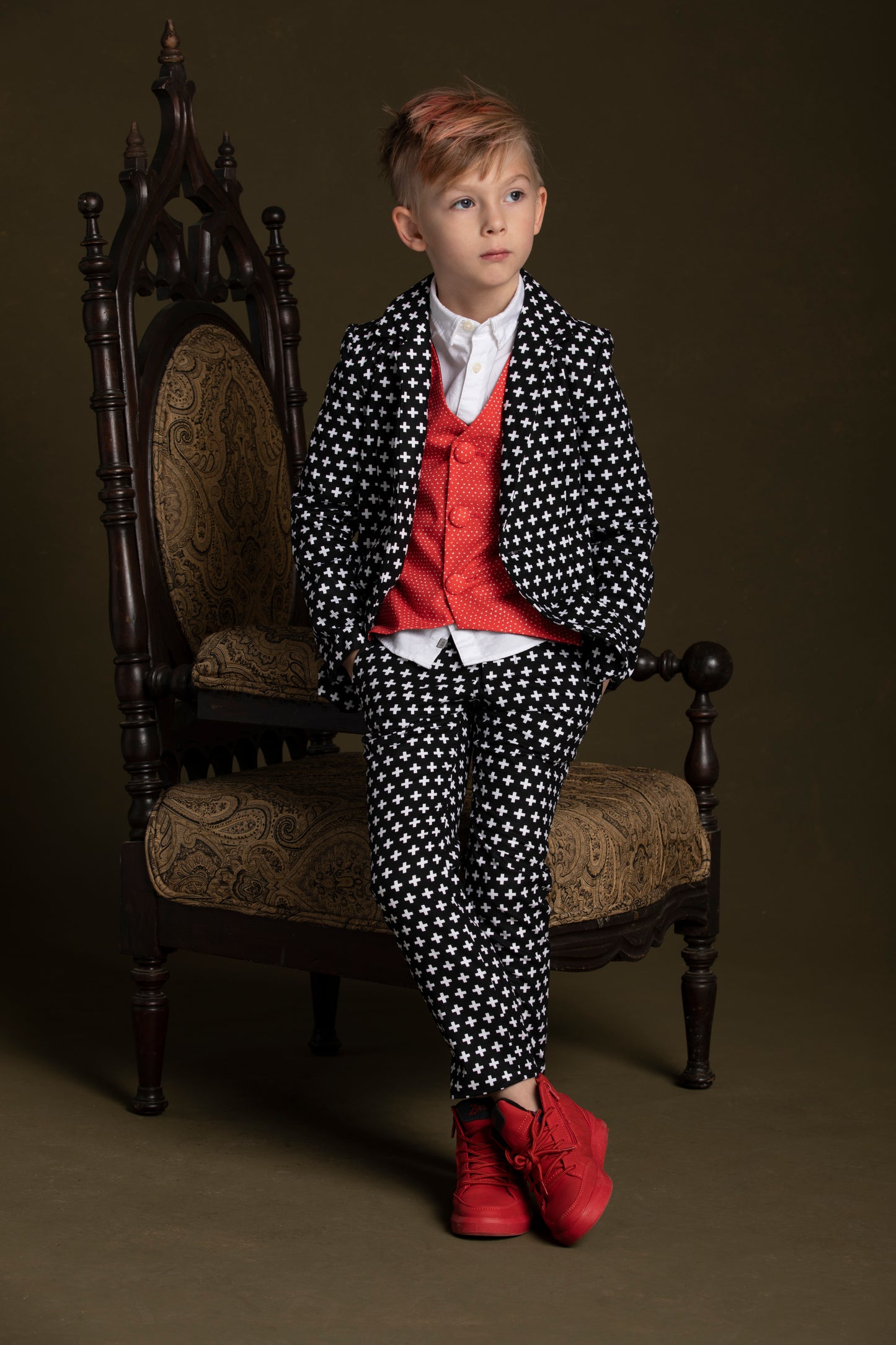 Young man leans against his chair in his red heart suit vest coordinated with the plus print suit